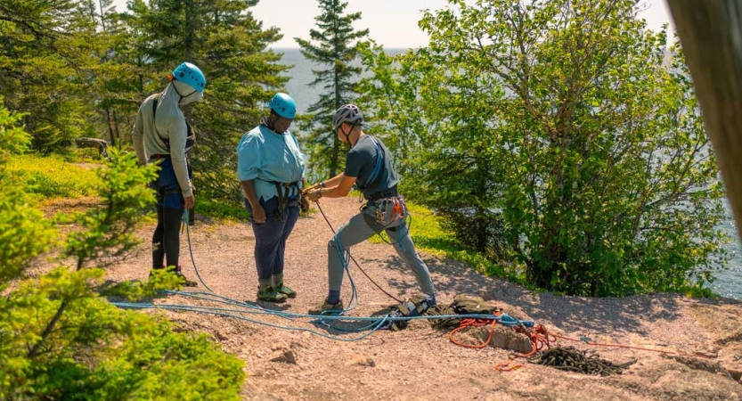 An instructor checks the safety gear of a student while another looks on. 